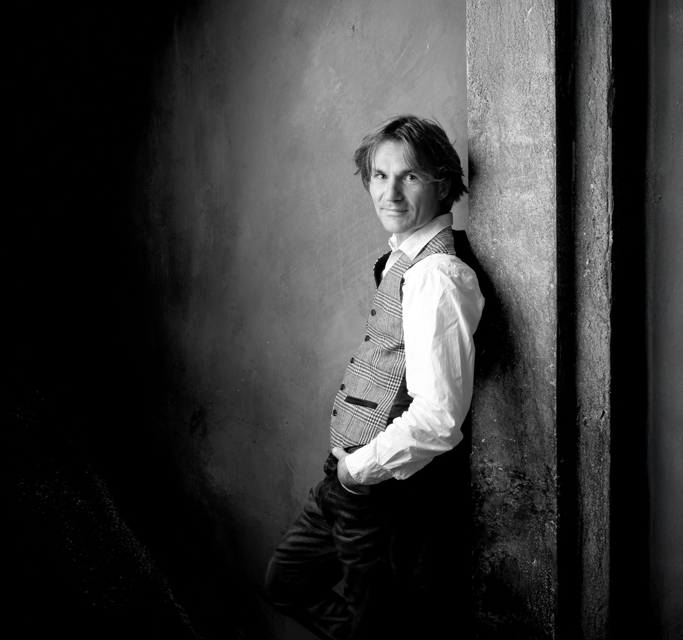 Ein Schwarz-Weiß-Foto von Michael Droste-Laux, der an einer Wand lehnt.